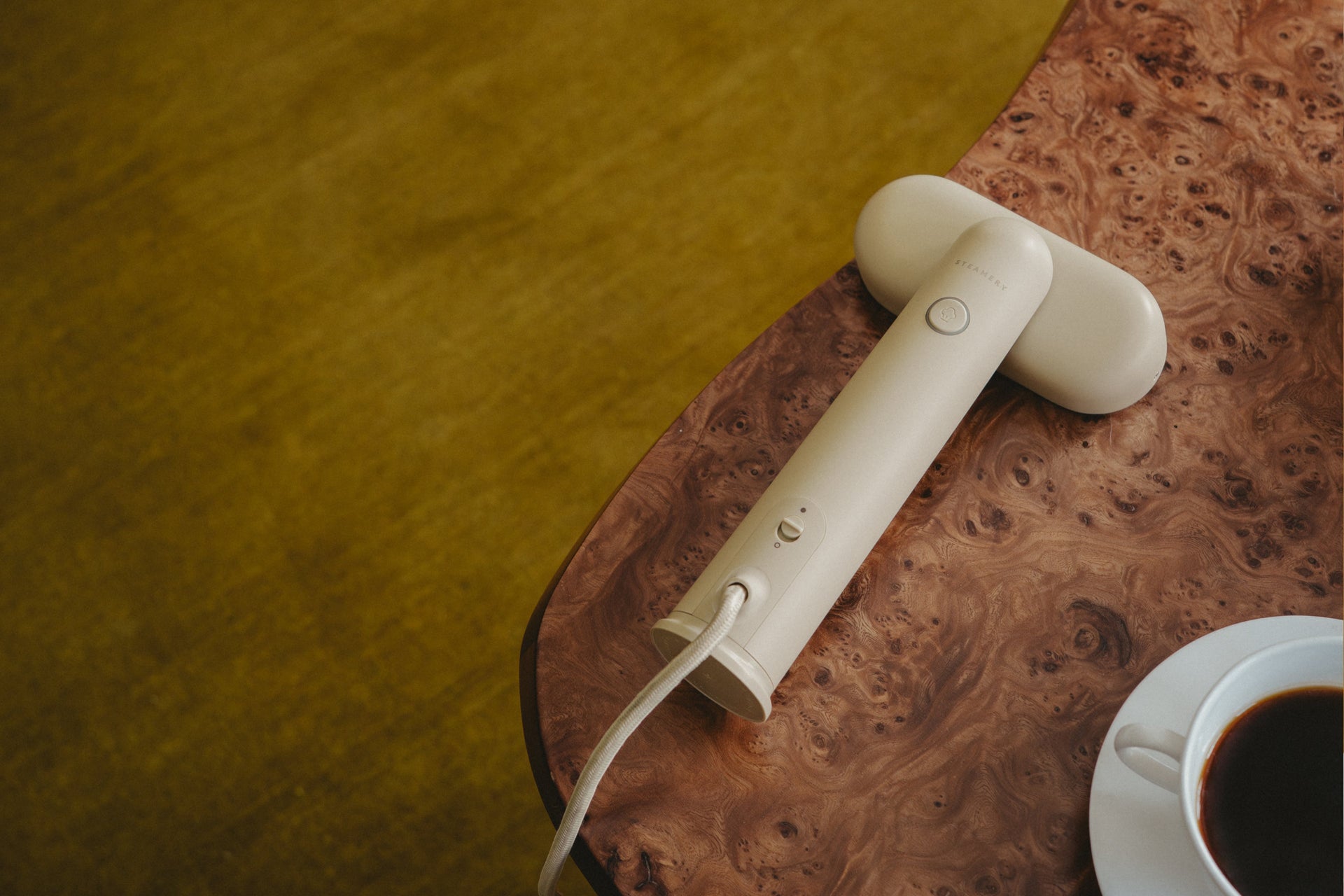 White travel steamer on a wooden surface with a cup of coffee