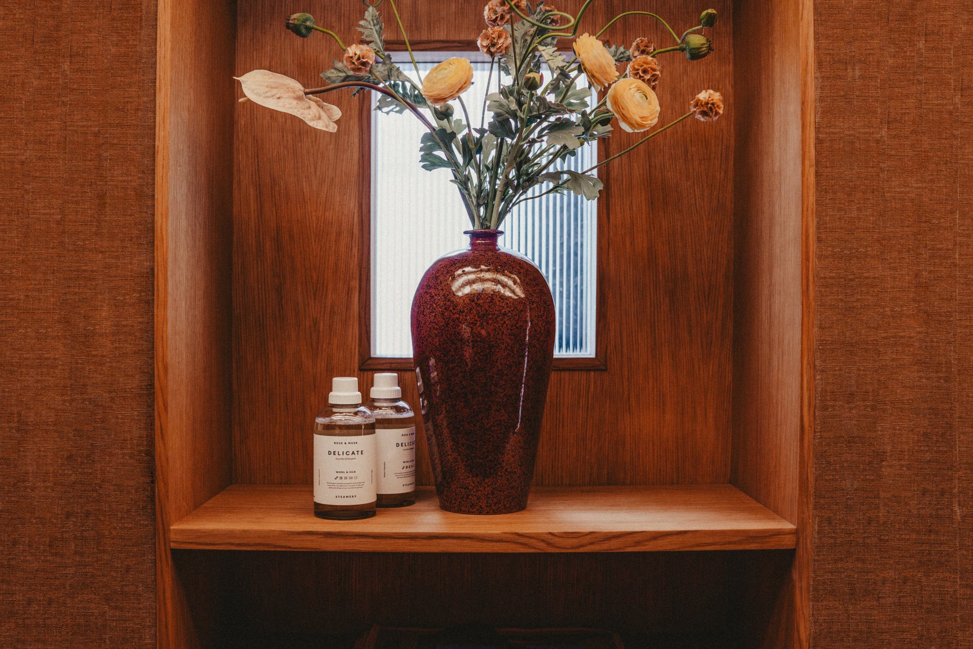 2 detergent bottles on a shelf next to flower vase