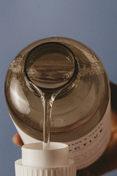 Clear liquid being poured from a brown bottle into a white container against a blue background