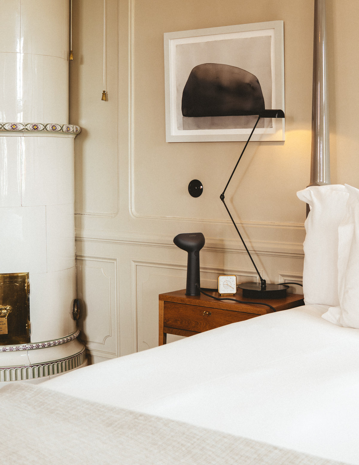 Bedroom scene with a handheld steamer on a nightstand, lamp, and framed picture on a wall.