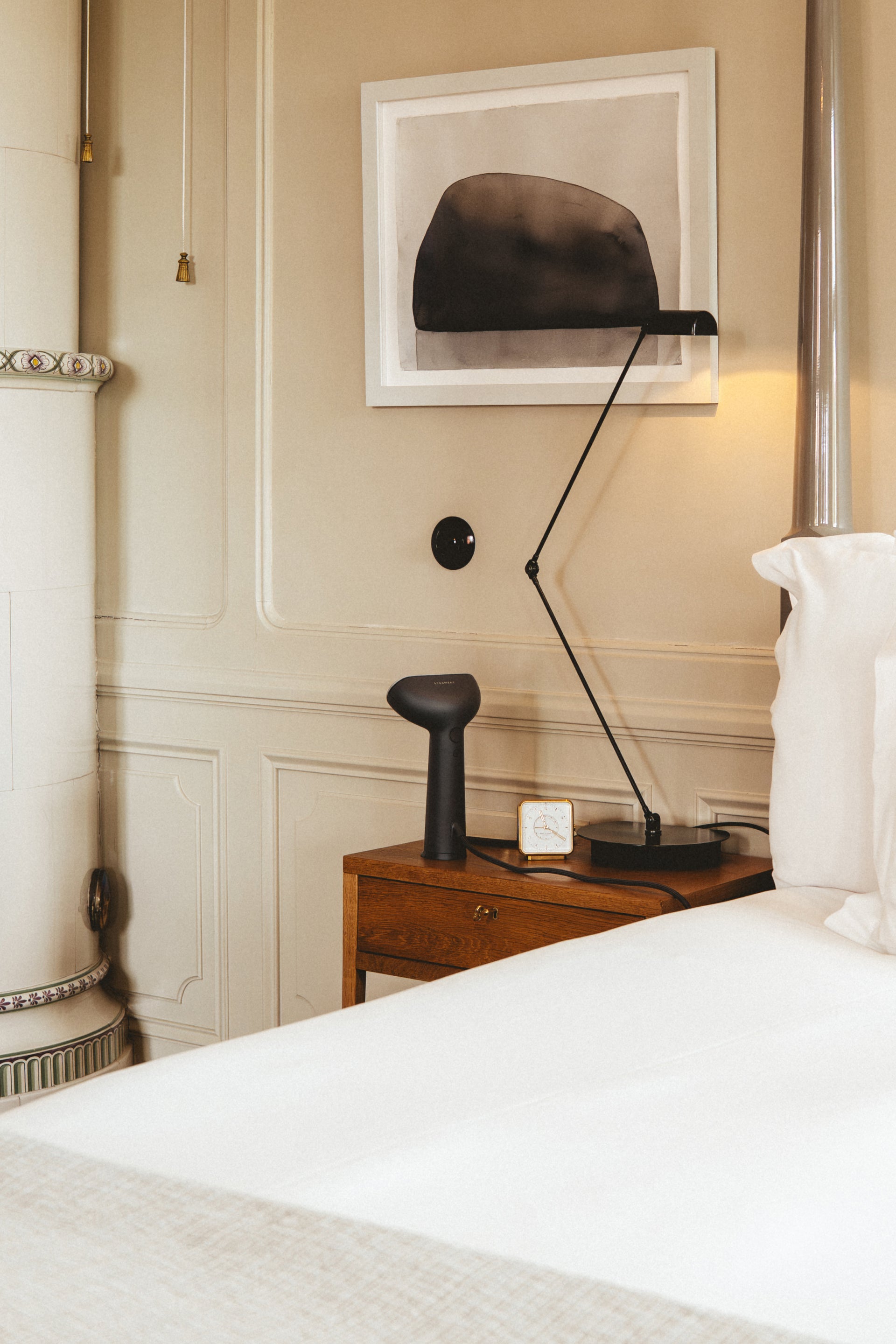 Bedroom scene with a handheld steamer on a nightstand, lamp, and framed picture on a wall.