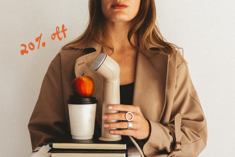 woman carrying a beige steamer, coffee cup and apple on a stack of books and binders