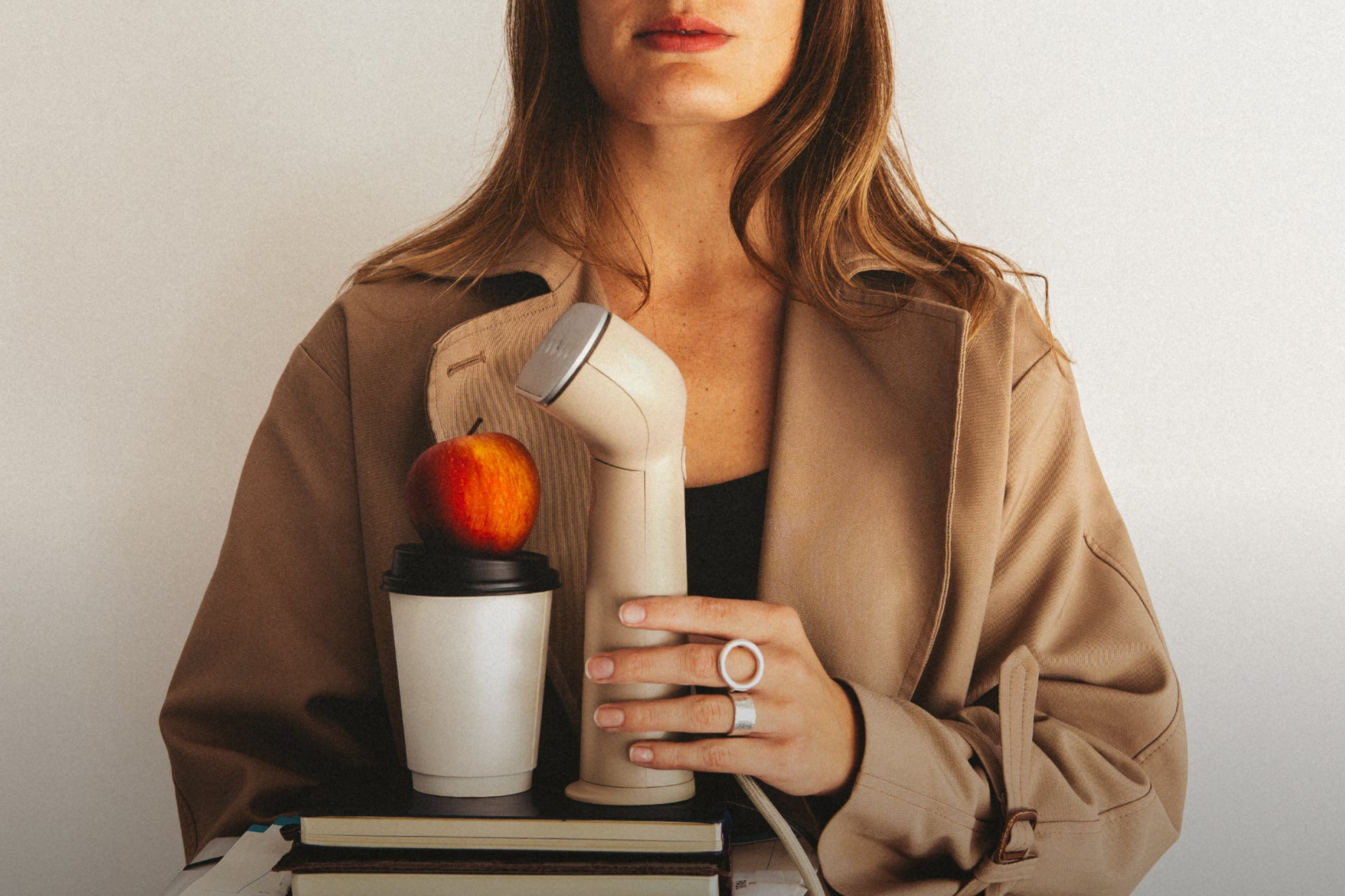 woman carrying a beige steamer, coffee cup and apple on a stack of books and binders