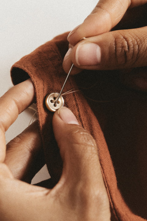 Person sewing a button onto a brown fabric with a neutral background