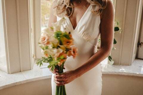 Woman in a white dress holding a bouquet of flowers indoors.