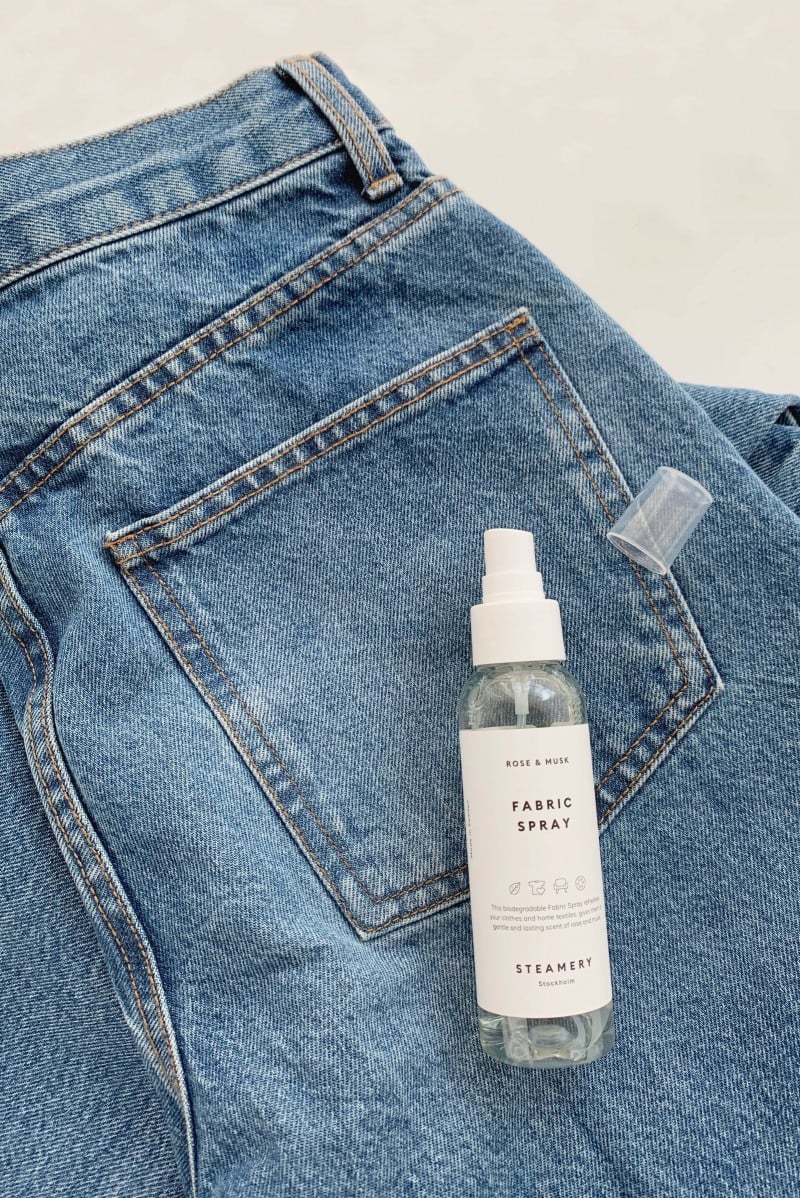 A 100 ml Fabric Spray laying on a pair of blue jeans