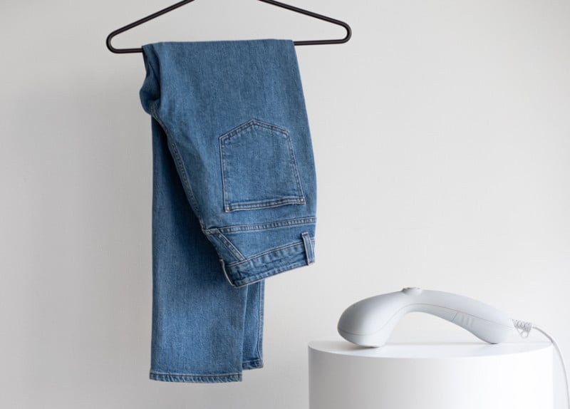 Blue jeans on a hanger next to a handheld steamer
