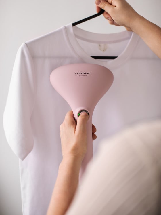 A person using the Steamery Cirrus 2 Handheld Steamer in Pink to steam a garment.